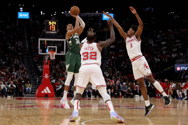 Giannis Antetokounmpo #34 of the Bucks shoots a three-point shot while defended by Amen Thompson #1 and Jeff Green #32 of the Rockets in the second half at Toyota Center on January 06, 2024 in Houston, Texas.