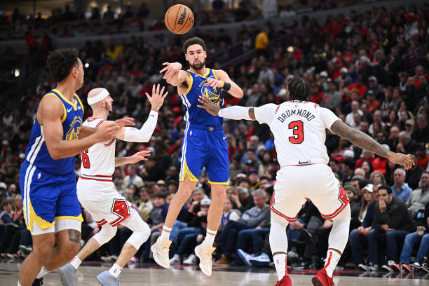 Klay Thompson #11 of the Warriors passes off to Trayce Jackson-Davis #32 while being defended by Alex Caruso #6 of the Chicago Bulls and Andre Drummond #3 at the United Center. 