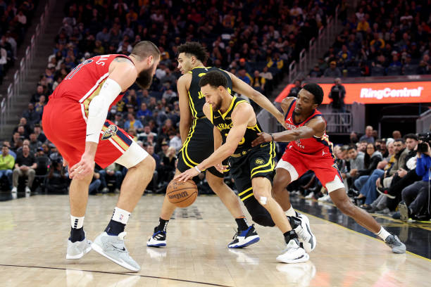 Stephen Curry of the Warriors dribbles past a pick set by Trayce Jackson-Davis. He is guarded by Herbert Jones and Jonas Valanciunas of the Pelicans at Chase Center on January 10, 2024 in San Francisco.